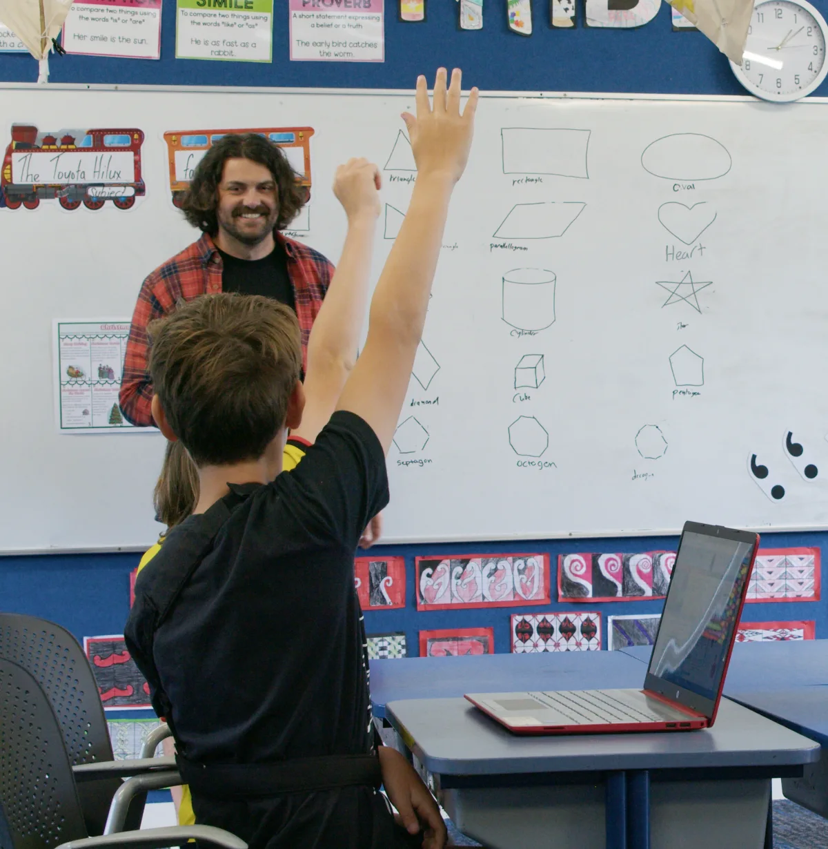 Teacher in Classroom with Students Raising hands on laptops